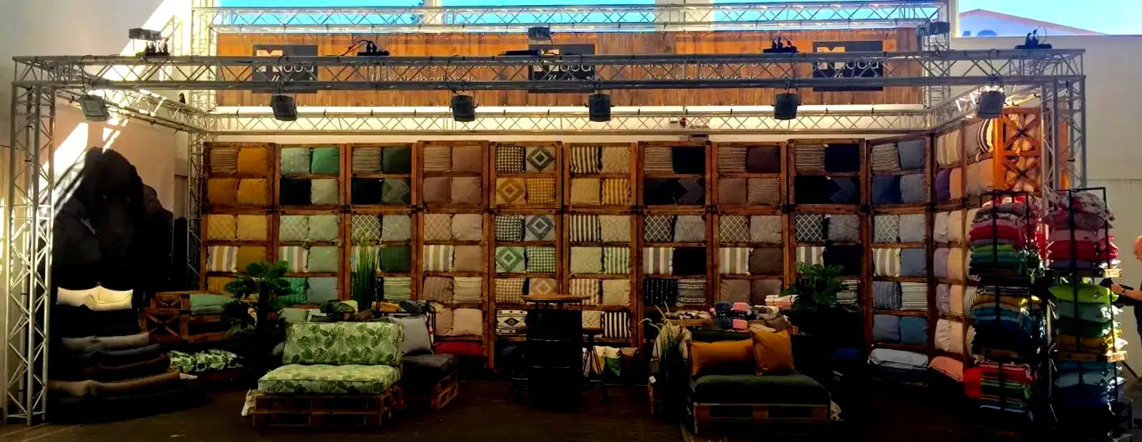 Trade fair stand with the collection wall: cushions and throws in wooden crates, set out on pallets.